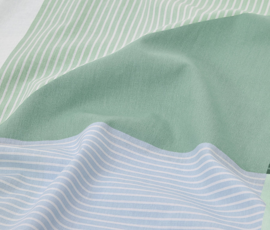 Zbliżenie na jasnoniebieską i zieloną pościel w paski.