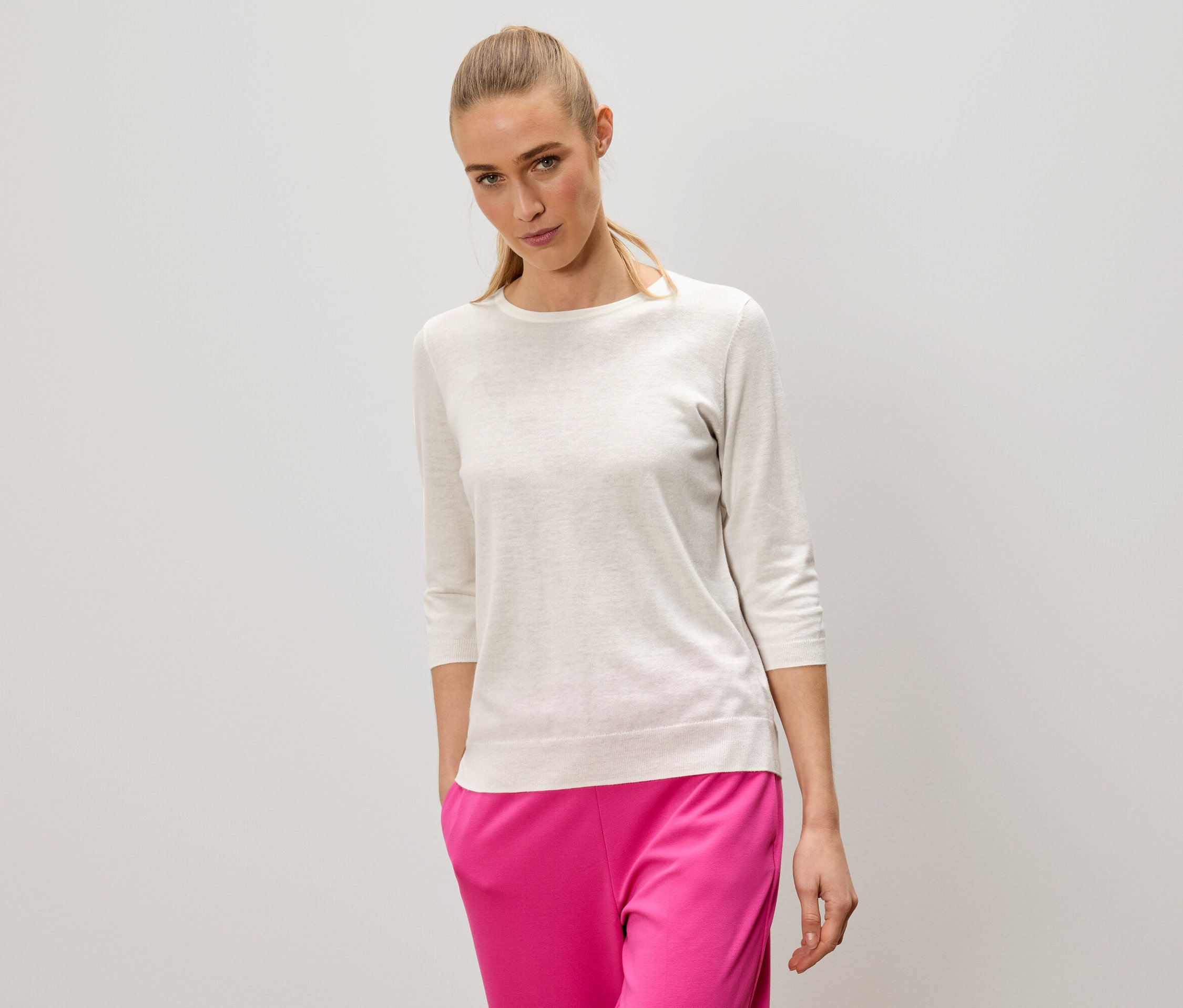 Kobieta o blond włosach ma na sobie jasny sweter i różowe spodnie.