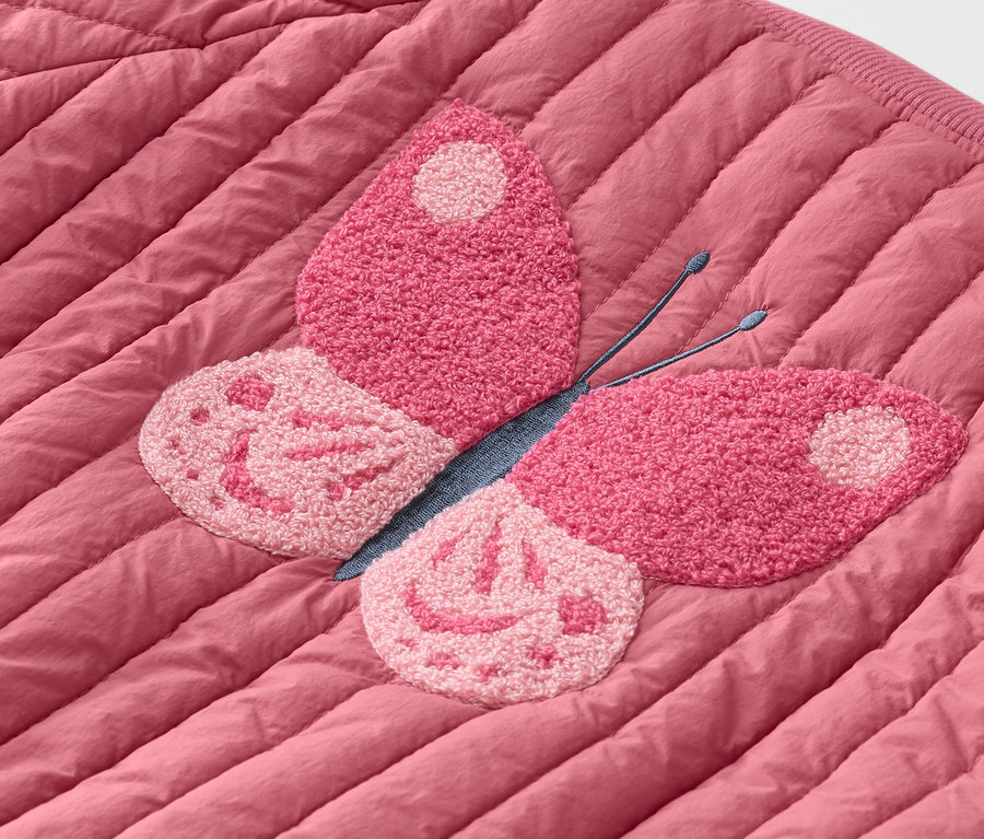 Zbliżenie na pikowaną, różową kurtkę z różową naszywką w kształcie motyla.