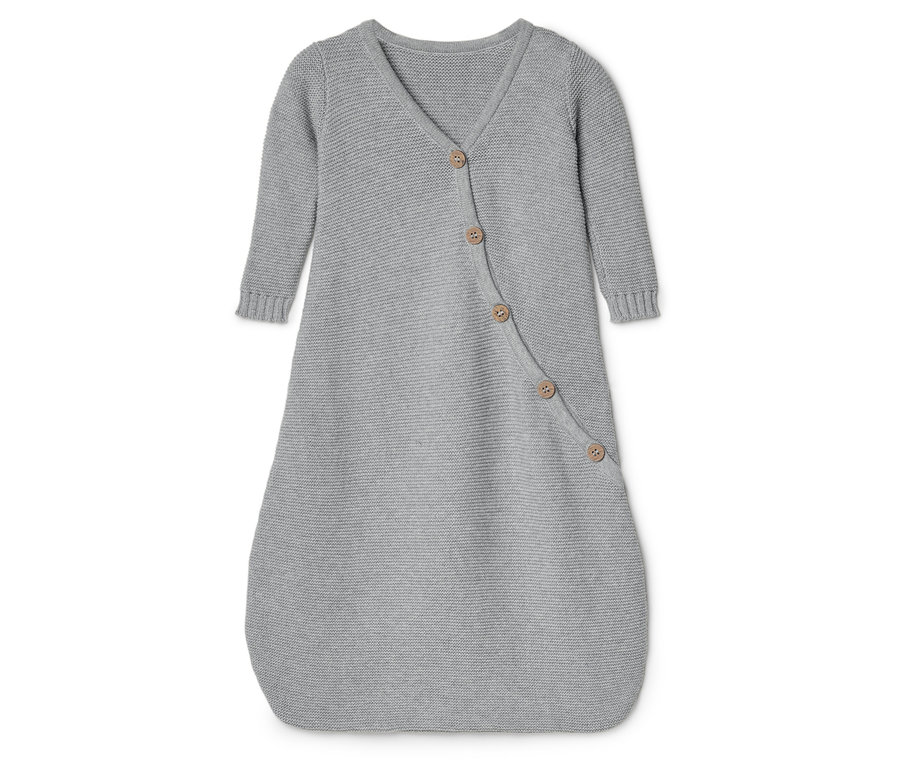 Szary, dziergany śpiworek dla niemowląt z długimi rękawami i zapięciem na guziki leży na białej powierzchni.