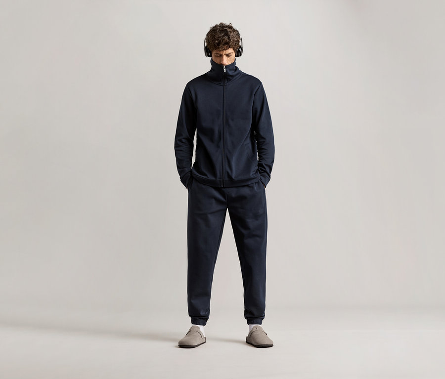 Mężczyzna w słuchawkach na uszach w granatowym dresie domowym.