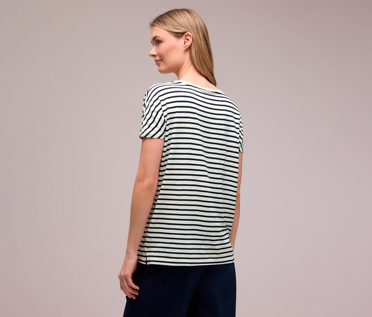 Kobieta z blond włosami, widziana z tyłu, ma na sobie granatowo-białą koszulkę Street One w poziome paski.