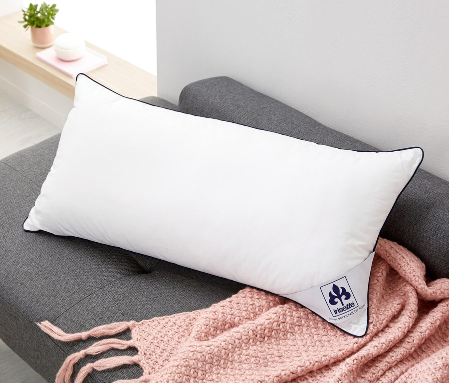 Poduszka regulująca temperaturę z bawełnianą poszewką, ok. 80 x 40 cm, leży na szarej sofie z różowym kocem.