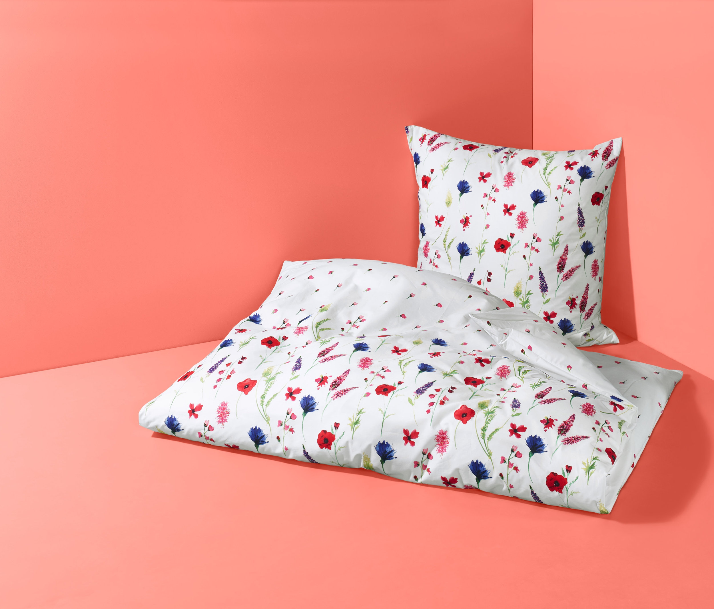 Biała, dwustronna pościel z perkalu w kwiaty, w rozmiarze podwójnym, leży na koralowym tle.