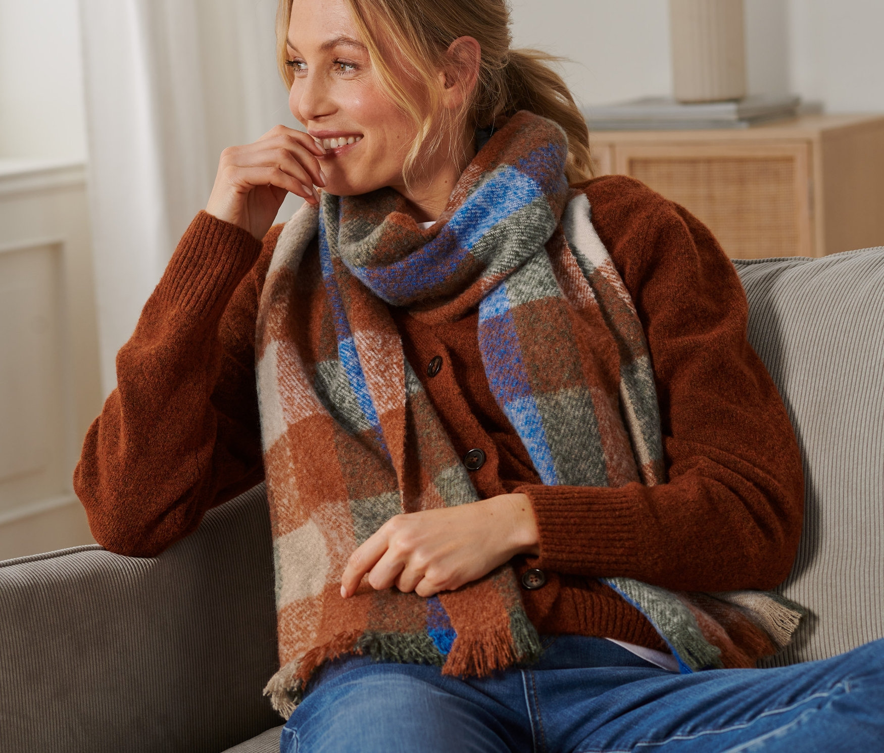 Kobieta siedzi na kanapie w szaliku z dzianiny w kratkę.