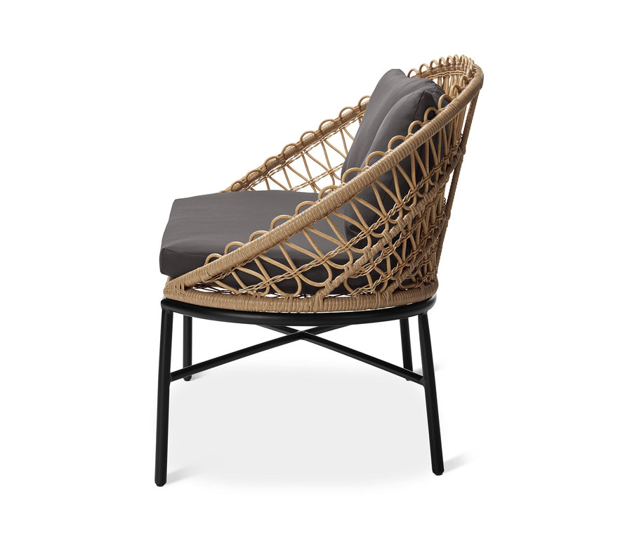 Boczny widok na stylową ławkę ogrodową z plecionką polirattanową i szarymi poduszkami.