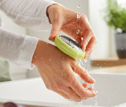 Kobieta myje ręce mydłem ze stali nierdzewnej z funkcją szczotki w białym zlewie.