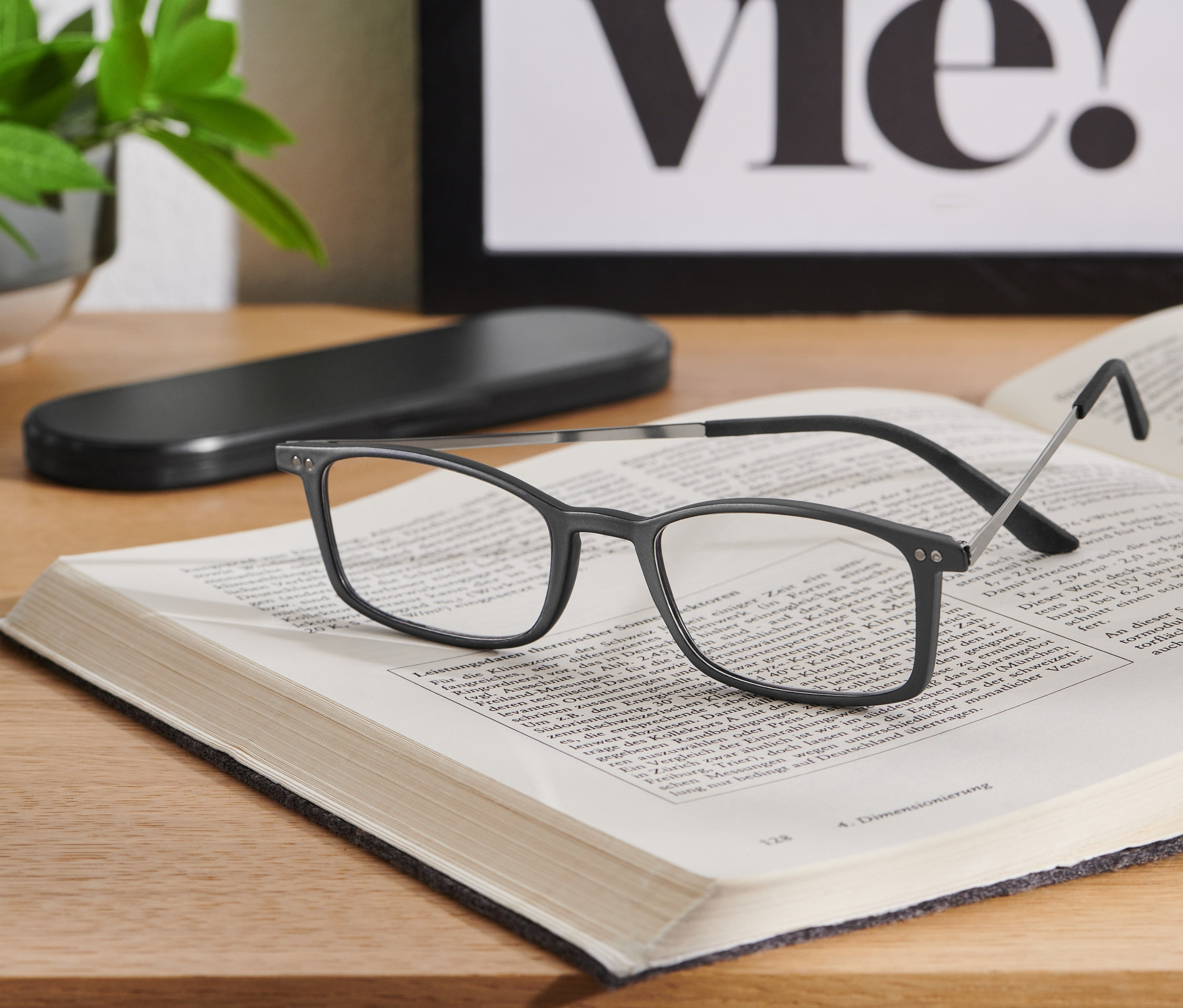 Czarne, ultra płaskie okulary do czytania leżą na otwartej książce na drewnianym stole.