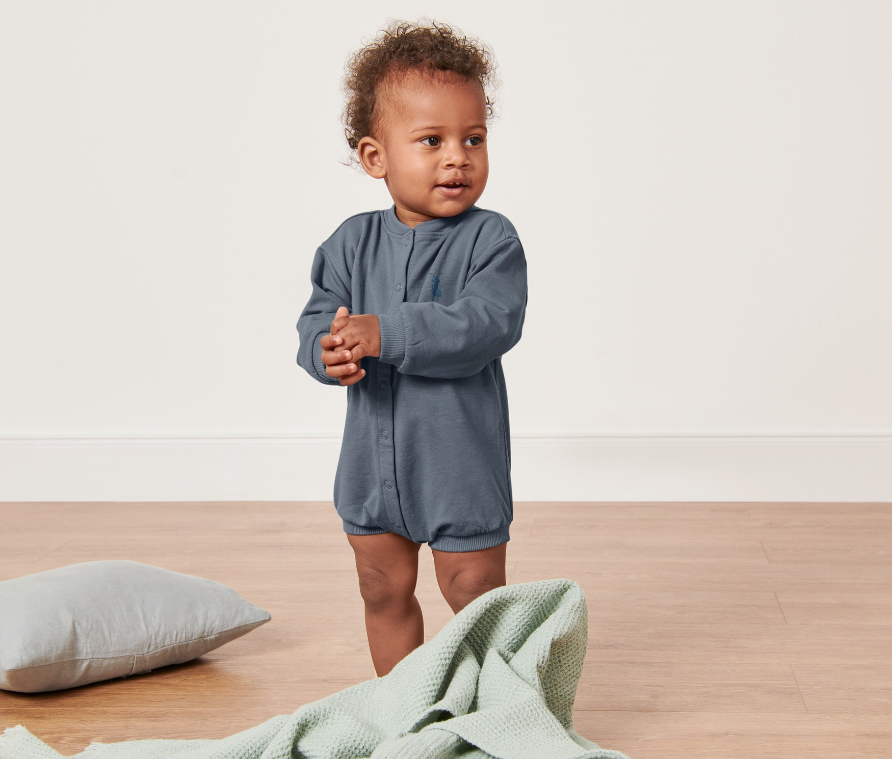 Dziecko stoi na podłodze w niebieskim body.