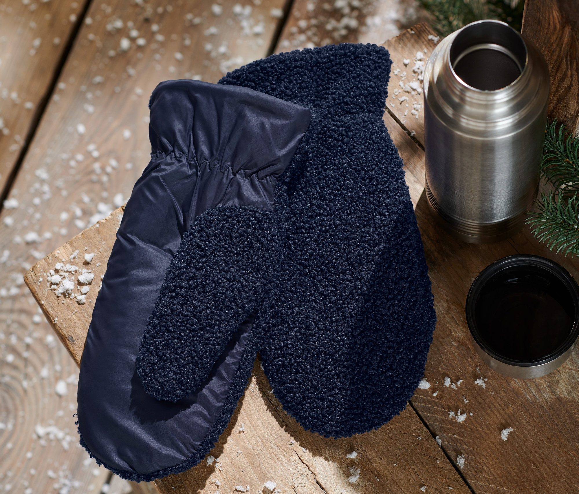 Na drewnianym stole leżą niebieskie rękawice-łapawice, termos i filiżanka.