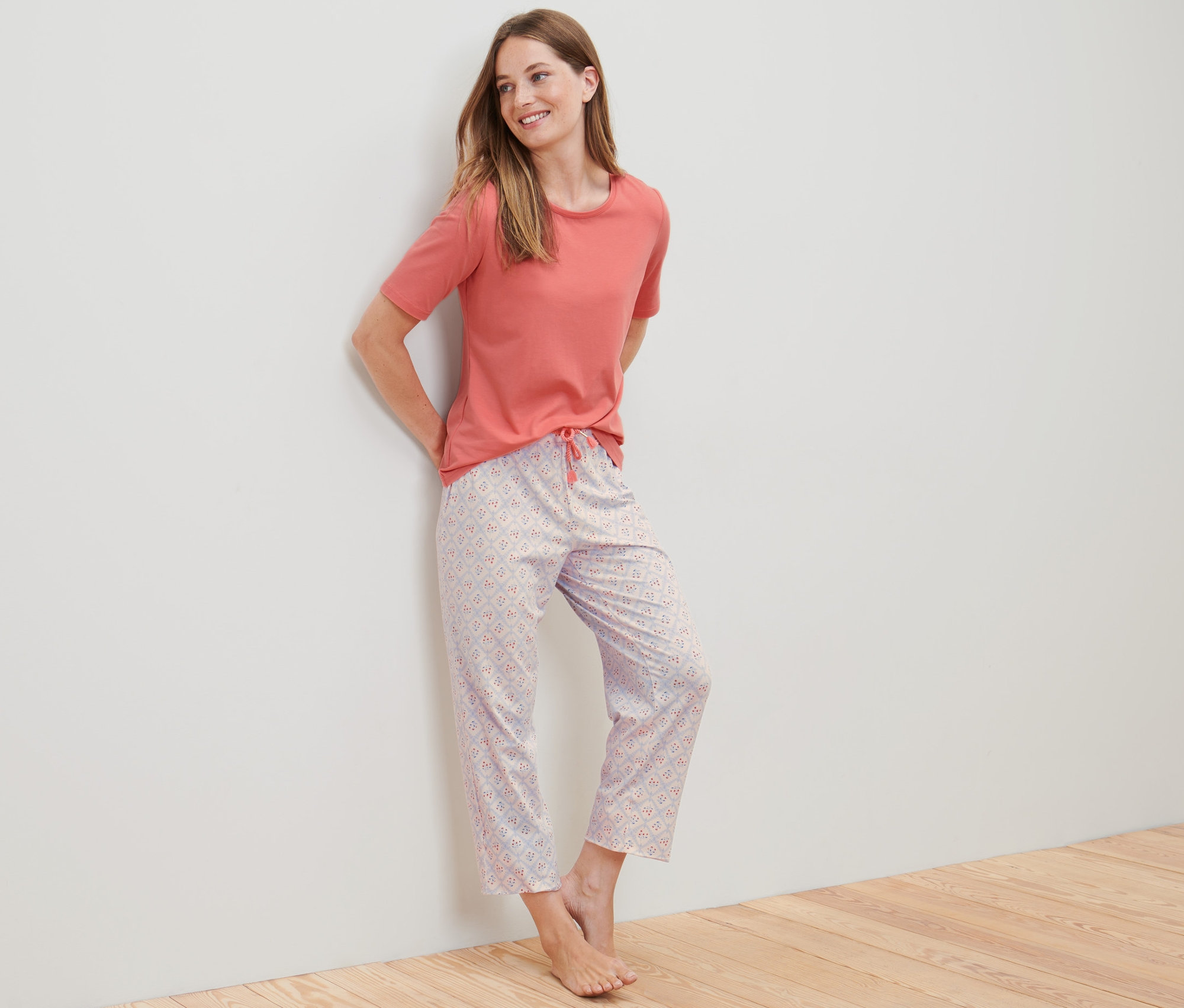 Kobieta opiera się o ścianę, ubrana w piżamę o długości 7/8.