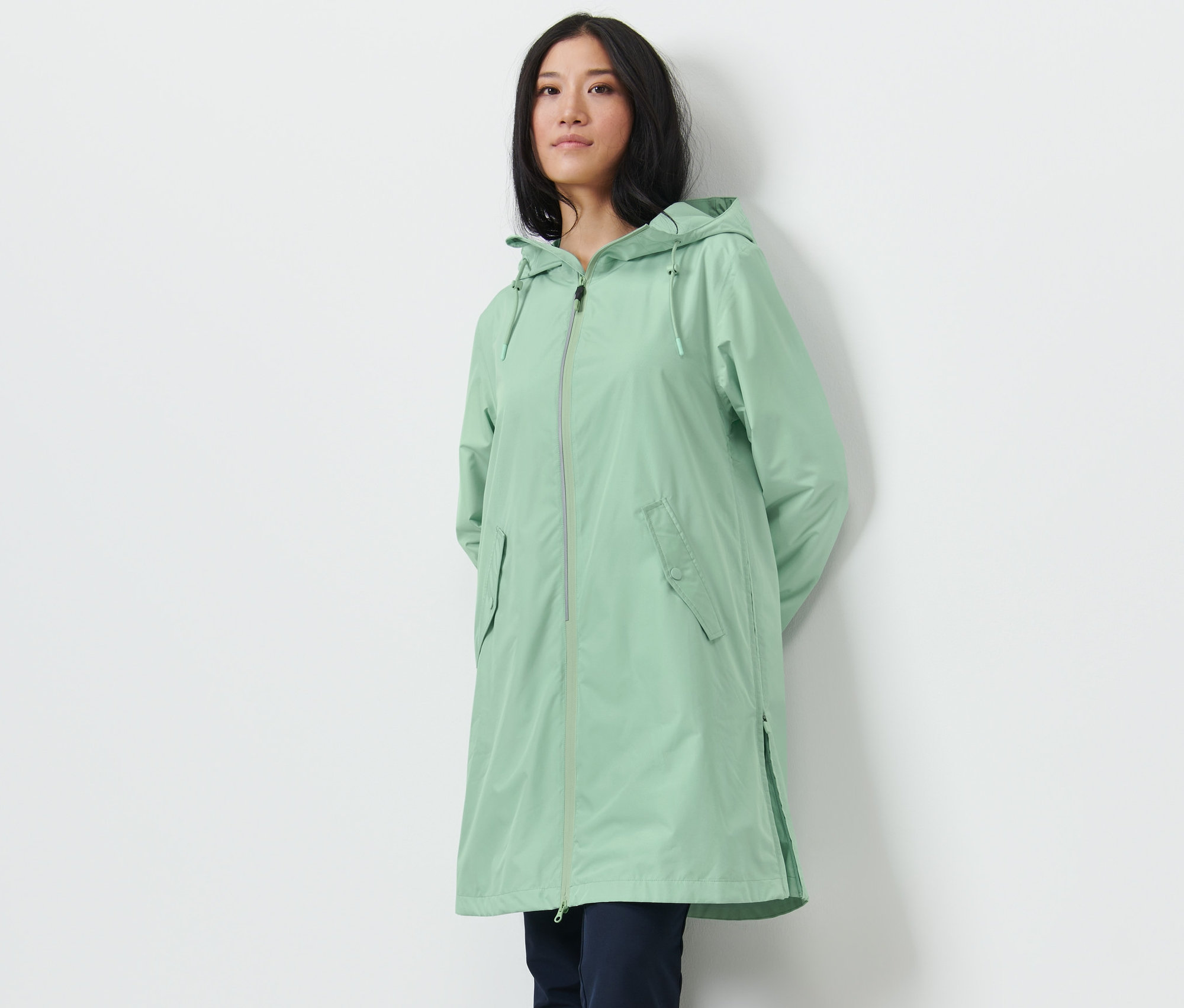 Kobieta pozuje w jasnozielonym płaszczu przeciwdeszczowym.