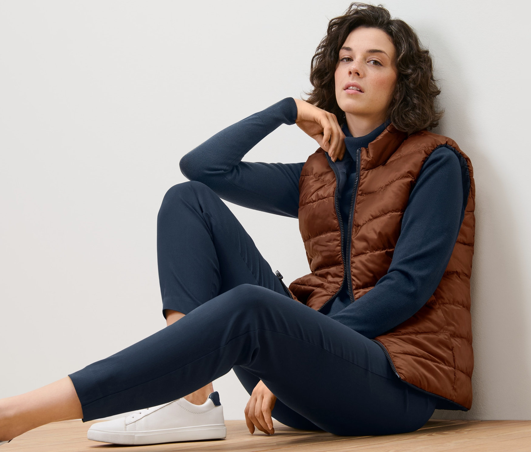 Kobieta siedzi na podłodze w dwustronnej kamizelce pikowanej.