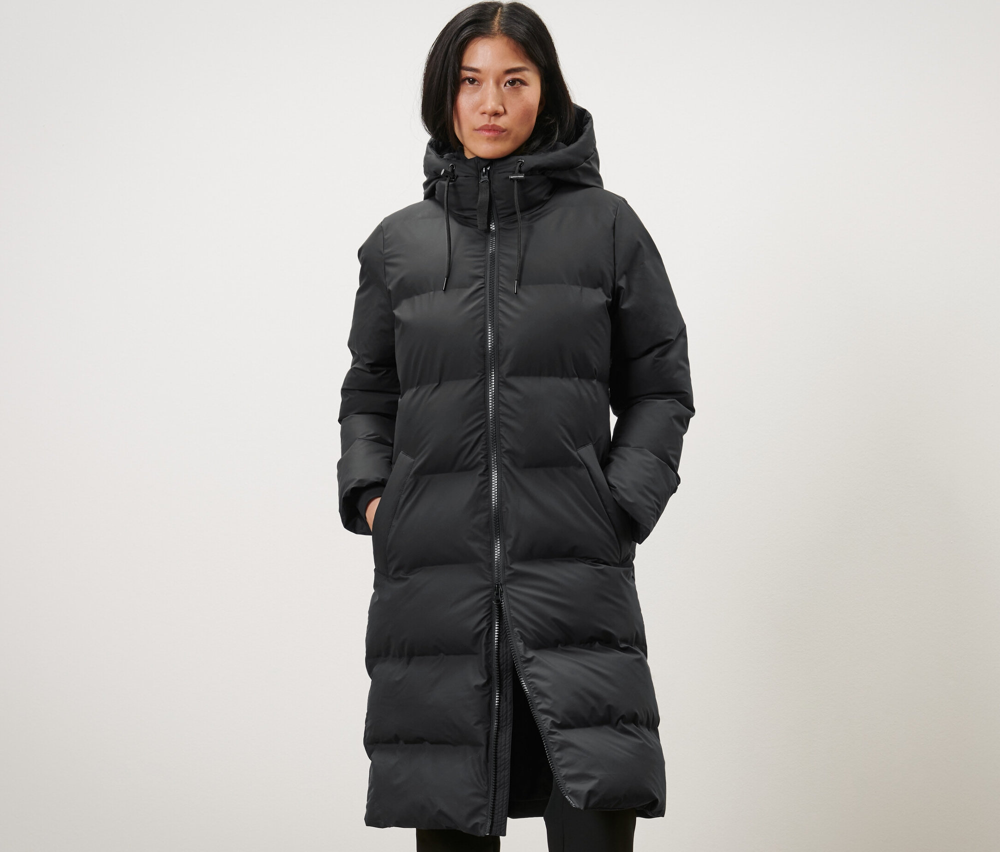 Kobieta ma na sobie długi, czarny zimowy płaszcz przeciwdeszczowy.