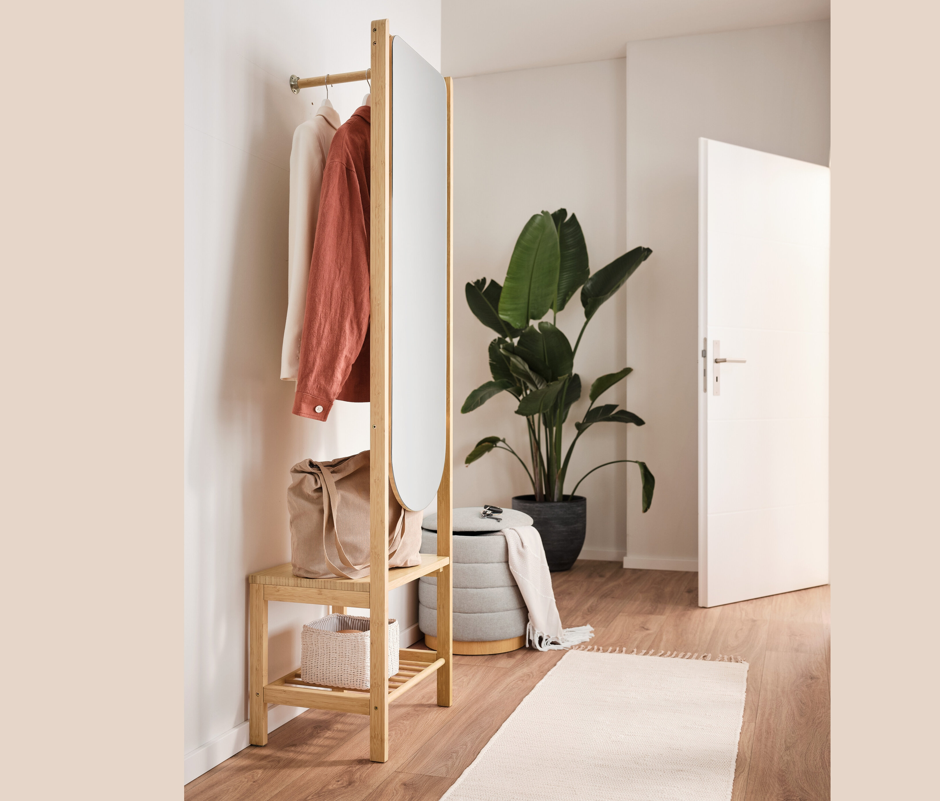 Wieszak na ubrania z lustrem i półką, puf ze schowkiem, torba i ubrania we wnętrzu.