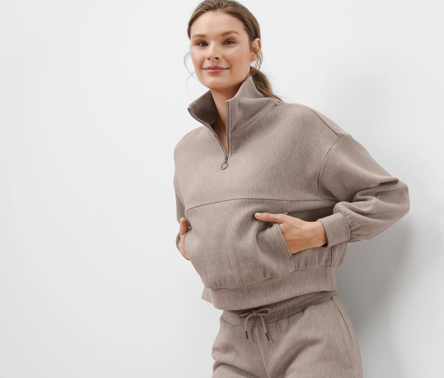 Kobieta pozuje w beżowej bluzie dresowej.