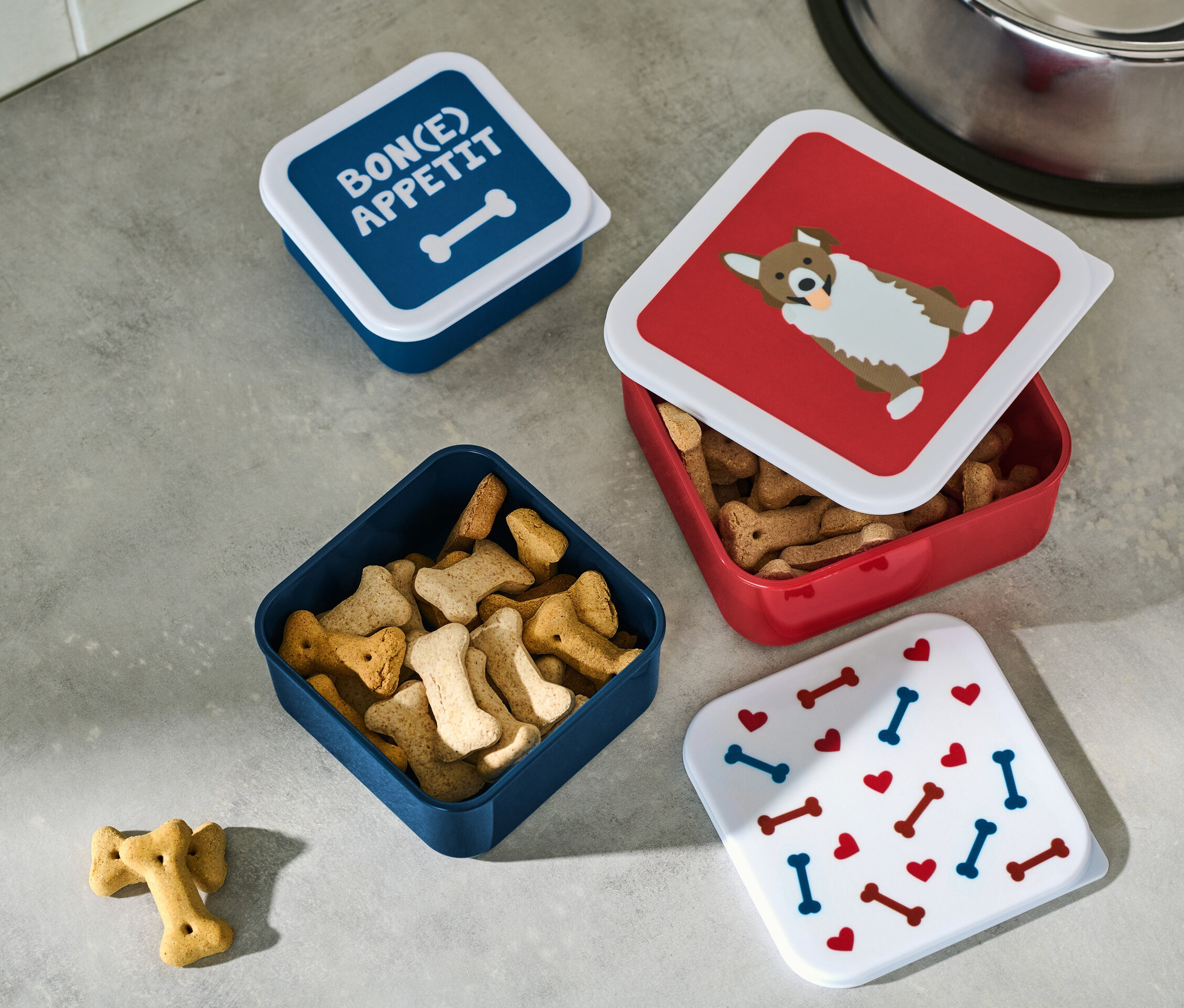 Cztery pojemniki na przekąski leżą na szarej powierzchni, jeden z nich jest otwarty i wypełniony przekąskami.