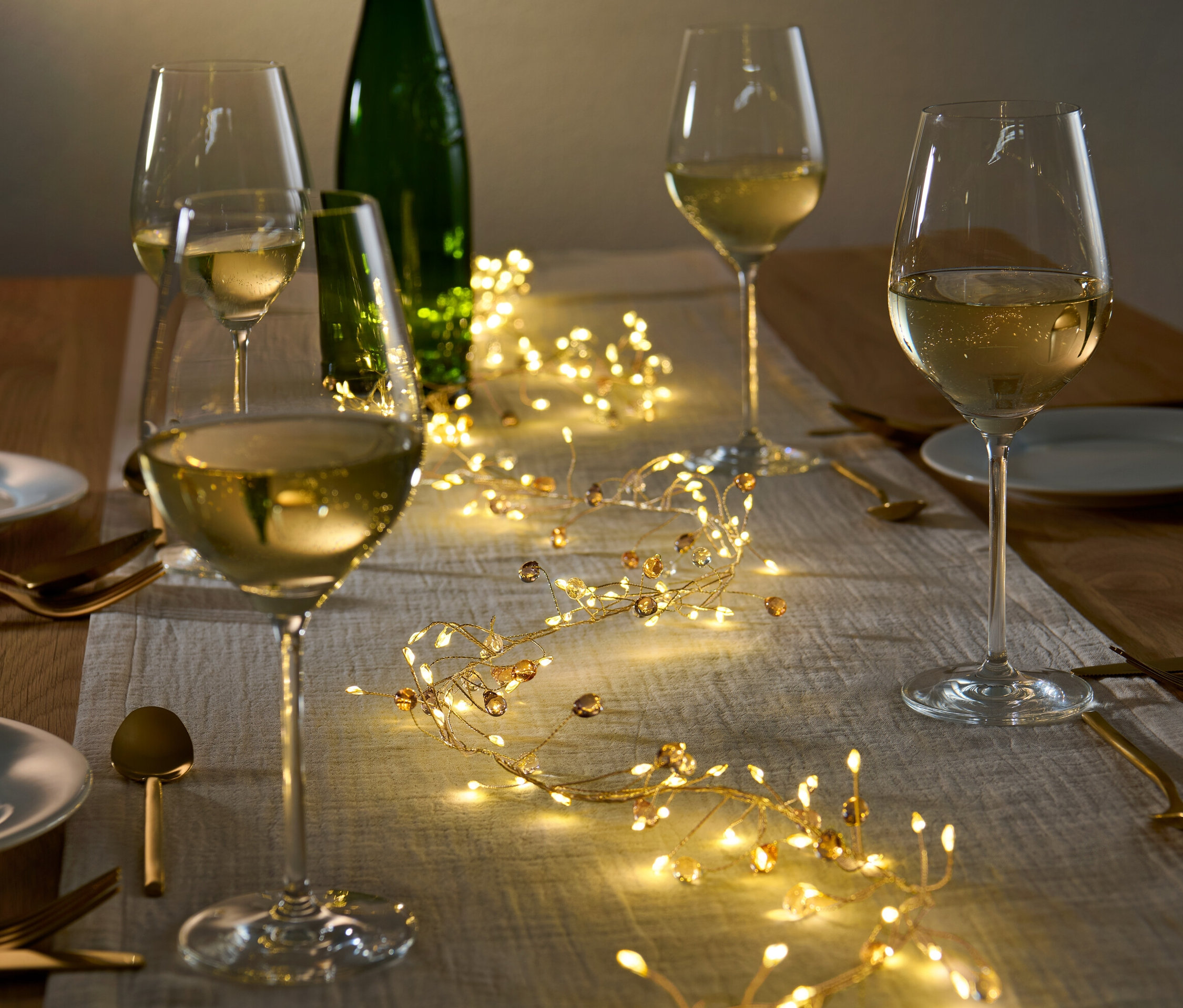 Stół z girlandą LED, kieliszkami do wina i talerzami.