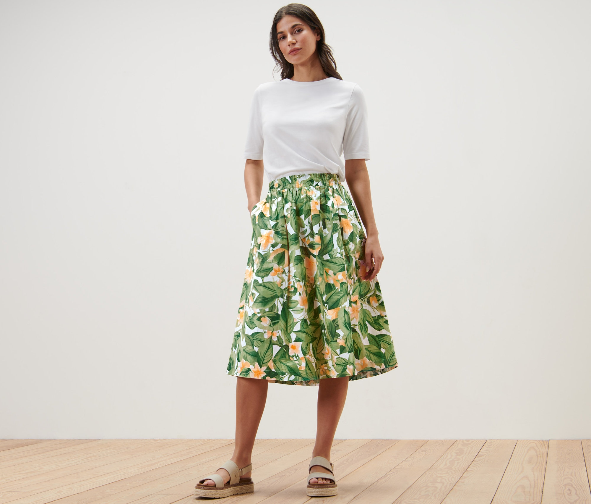 Kobieta pozuje w białym t-shircie i wzorzystej spódnicy z popeliny.