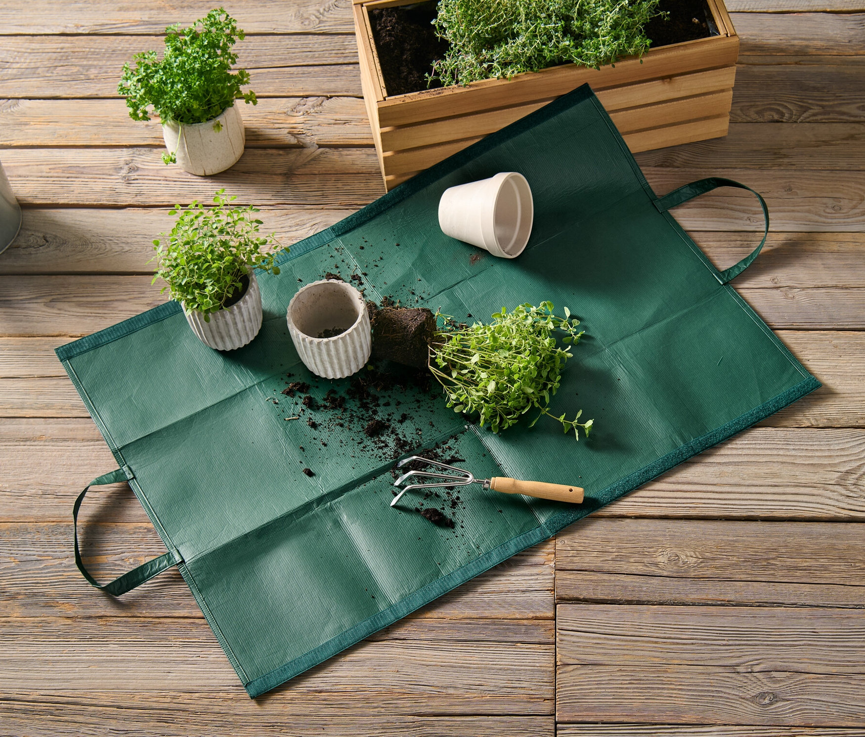 Torba na odpady ogrodowe leży na drewnianej podłodze obok roślin doniczkowych i konewki.