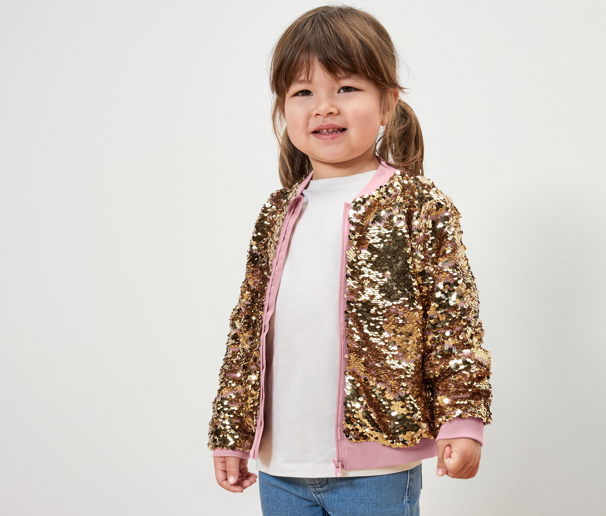 Uśmiechnięta dziewczynka pozuje w bluzie rozpinanej z cekinami.