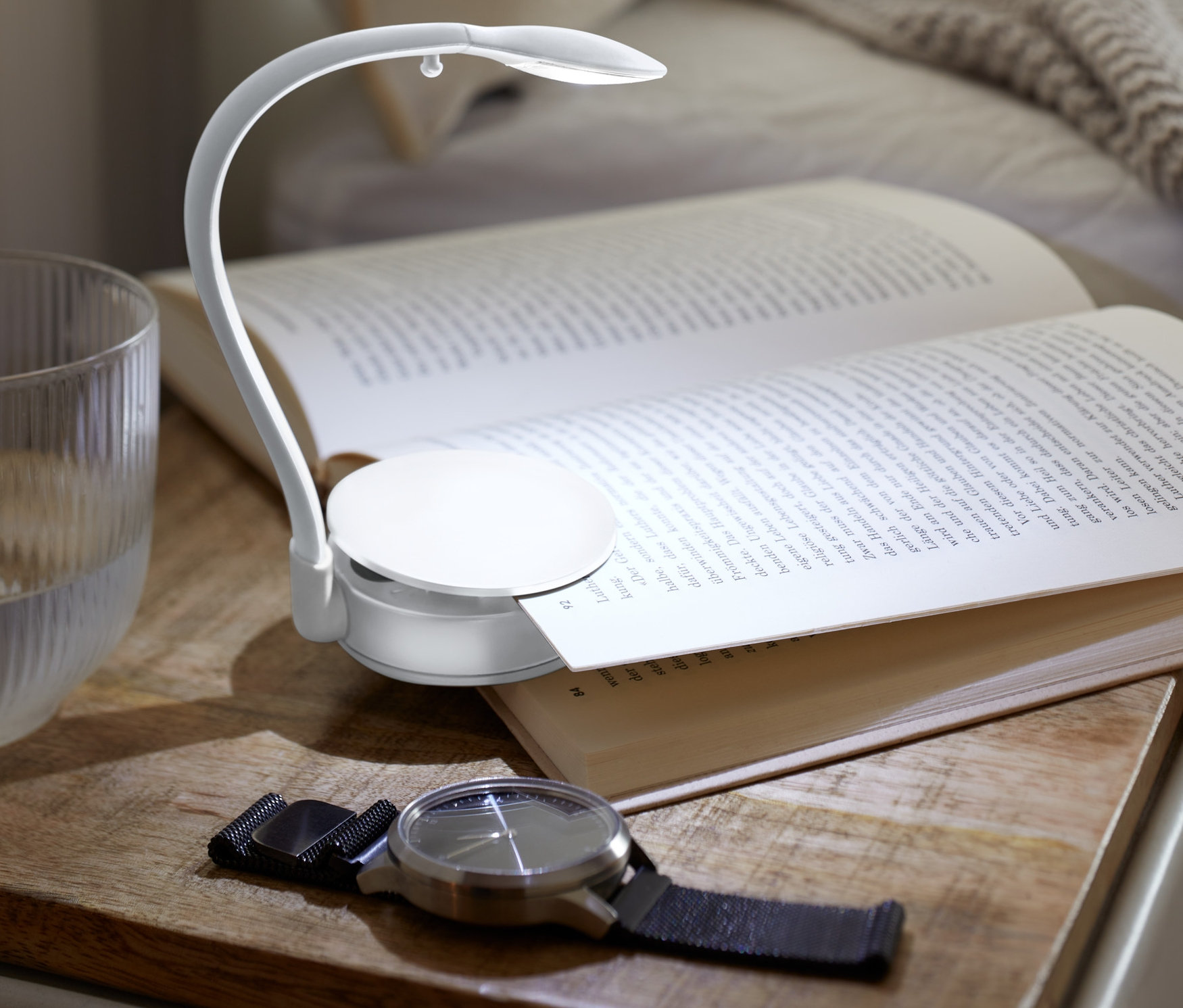 Otwarta książka leży na szafce nocnej oświetlona lampką LED do czytania.