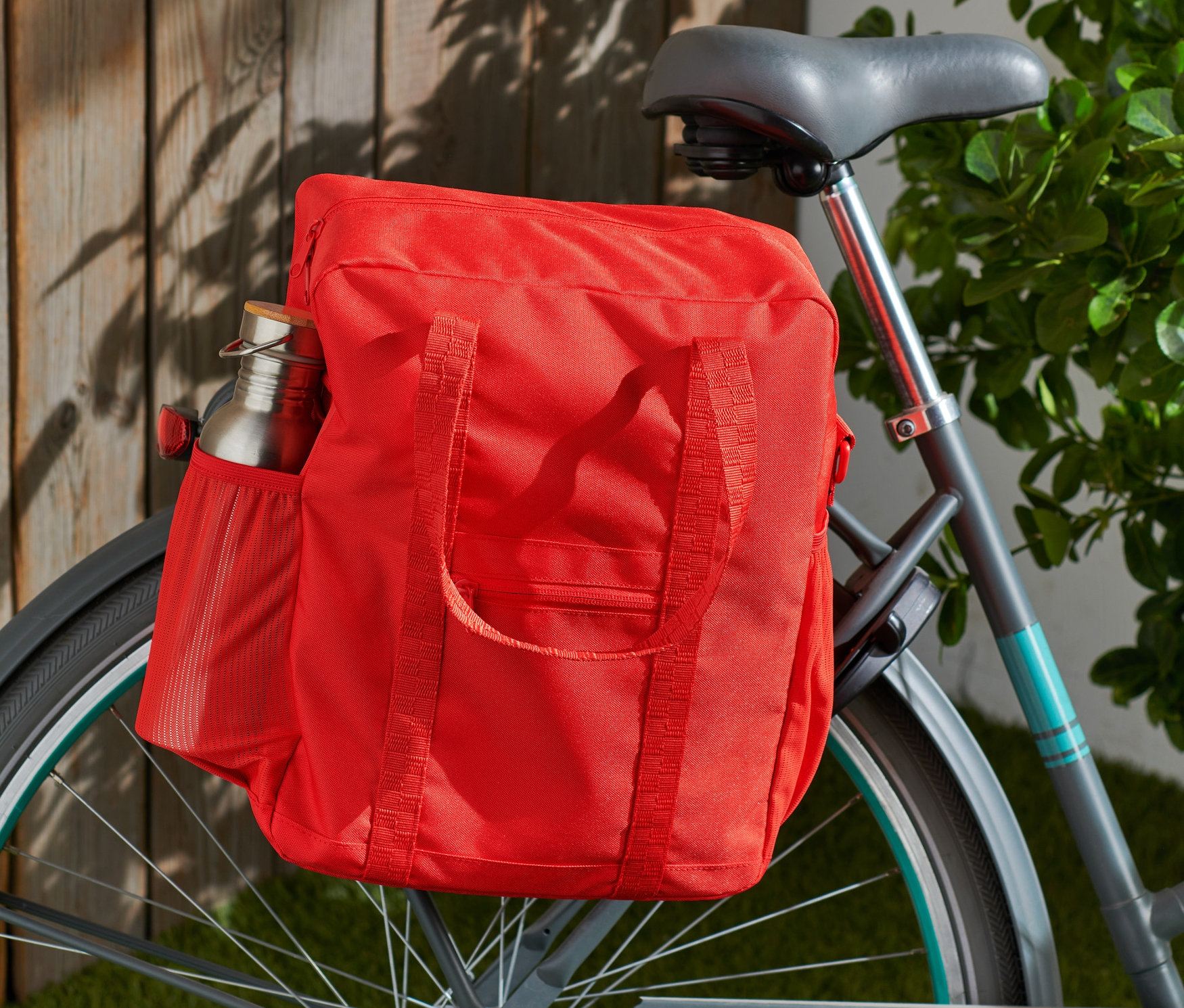 Czerwona torba na rower i do przewieszenia przez ramię przymocowana jest do roweru.