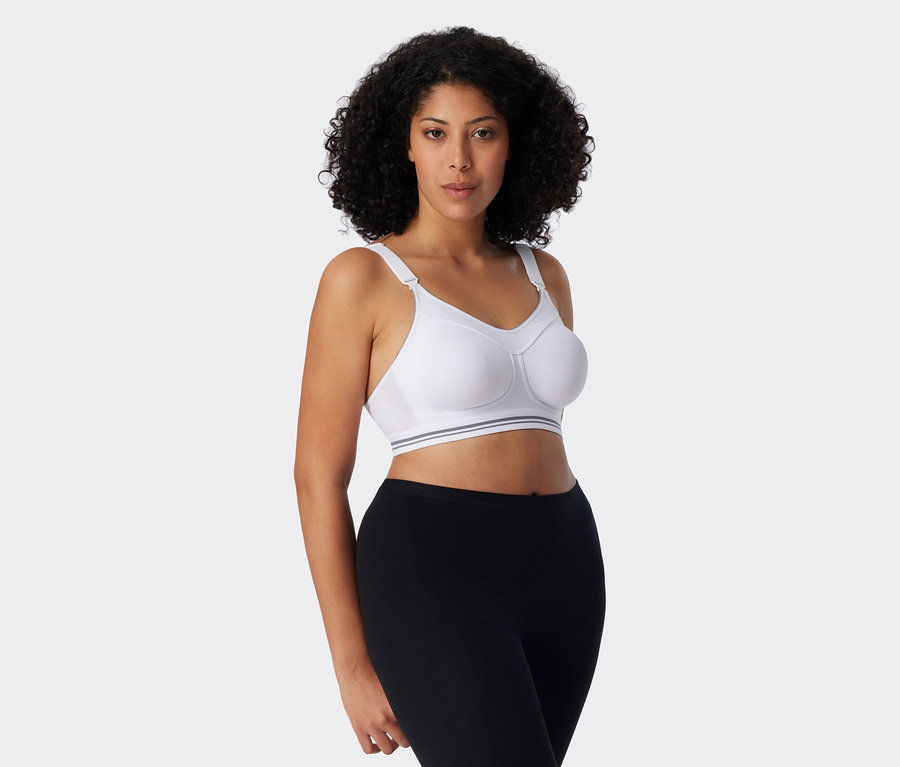 Kobieta z kręconymi włosami ma na sobie biały biustonosz sportowy i czarne legginsy.