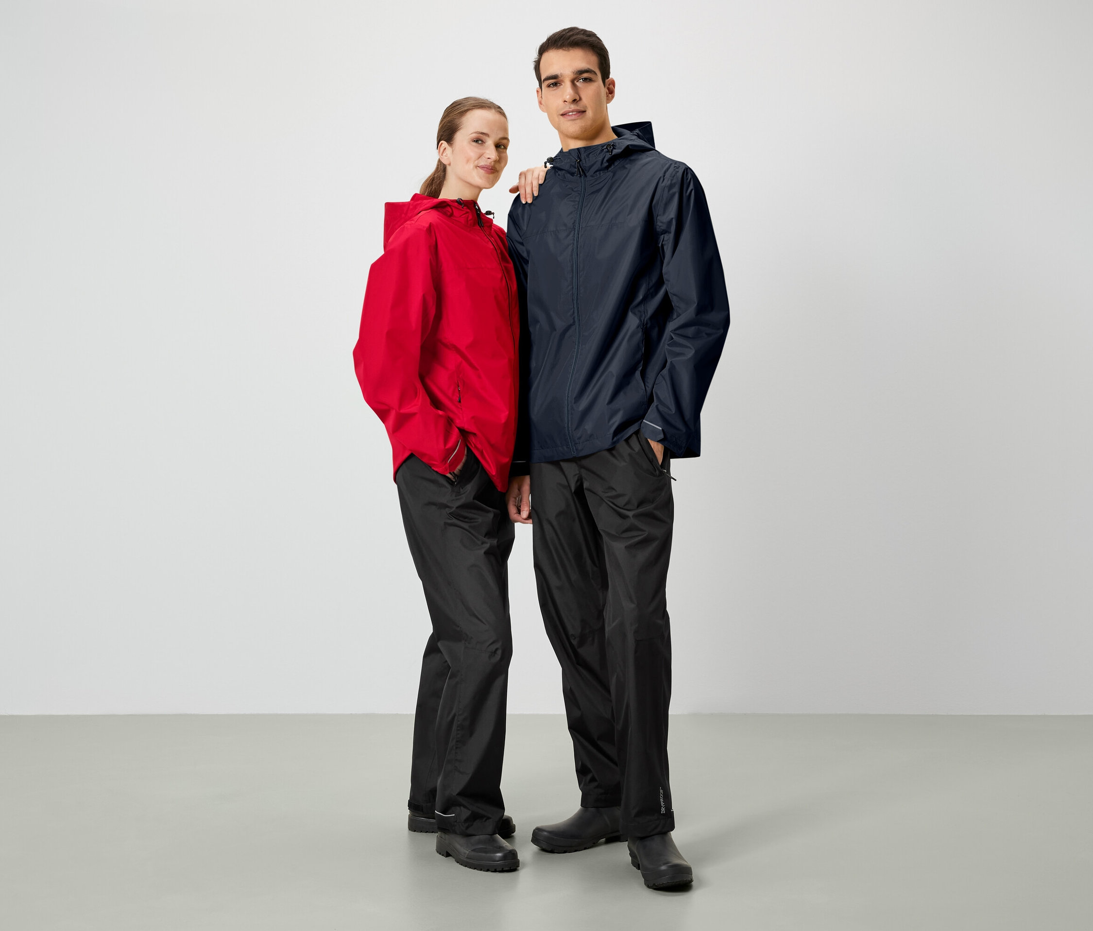 Mężczyzna i kobieta pozują obok siebie. Oboje mają na sobie kurtki przeciwdeszczowe i czarne spodnie.