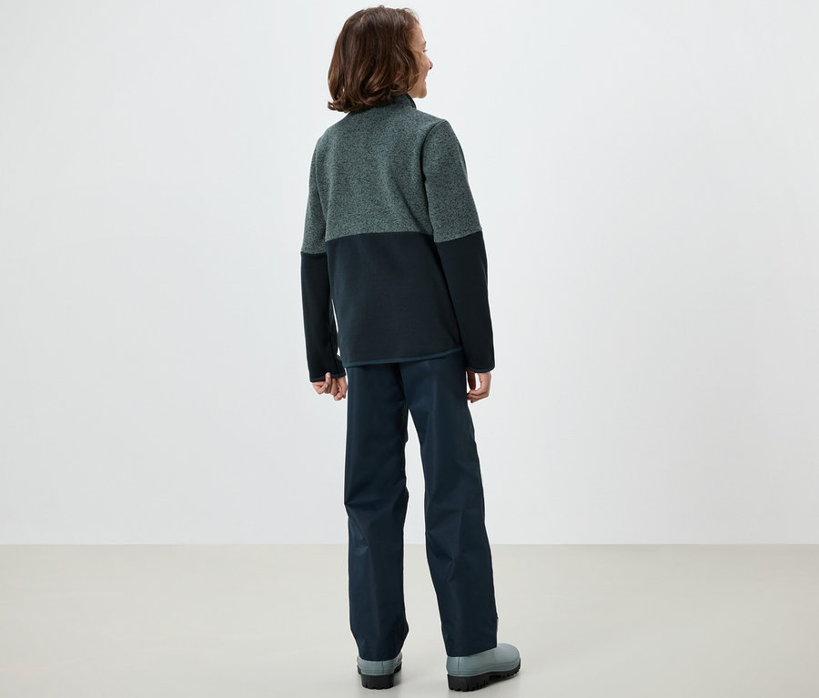 Chłopiec stoi tyłem, ubrany w polarową kurtkę hybrydową dla dzieci.