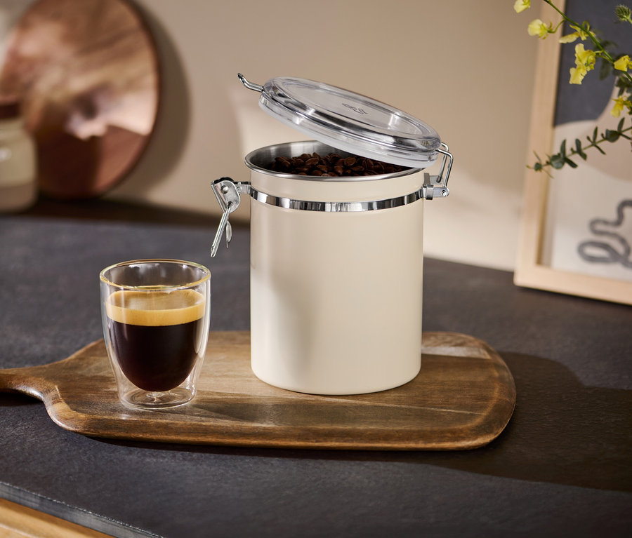 Otwarta beżowa puszka na aromat obok filiżanki espresso na drewnianej tacy.