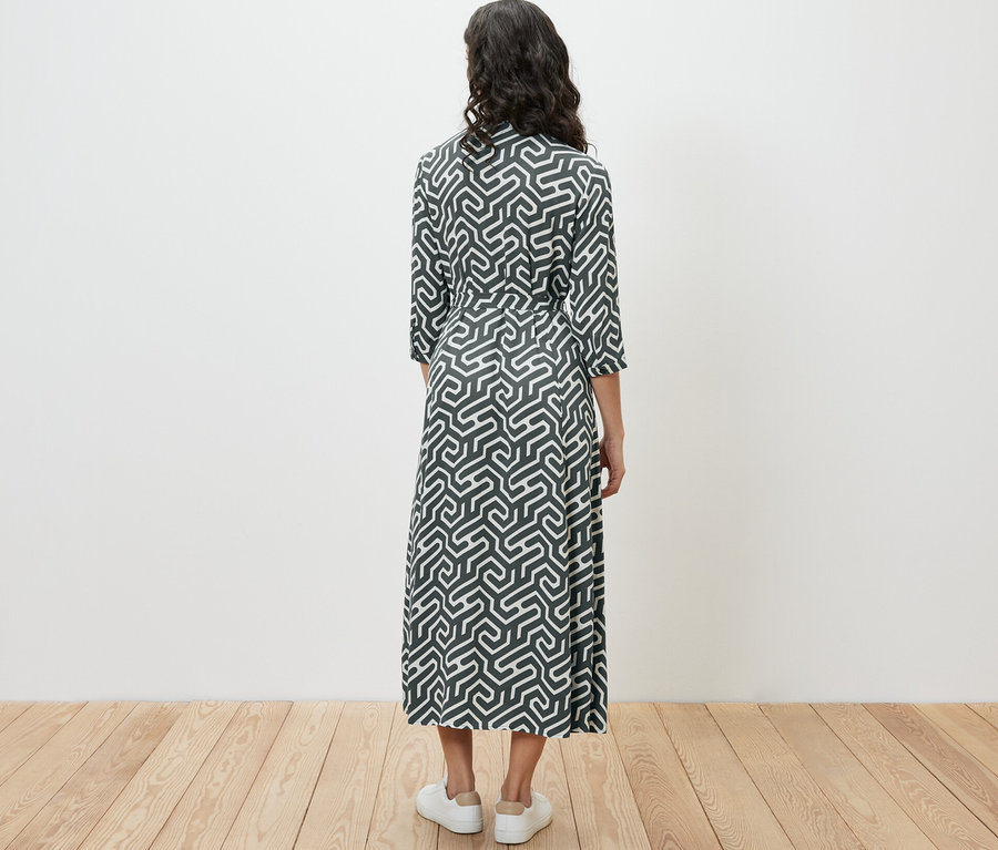 Kobieta stoi tyłem w sukience koszulowej.