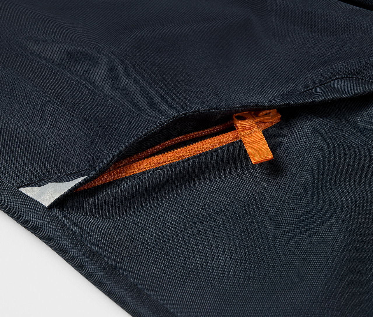 Zbliżenie na spodnie softshellowe dziecięce z pomarańczowym zamkiem błyskawicznym przy kieszeni.