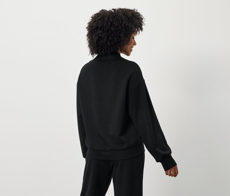 Widok z tyłu kobiety z kręconymi włosami w czarnej bluzie i spodniach.