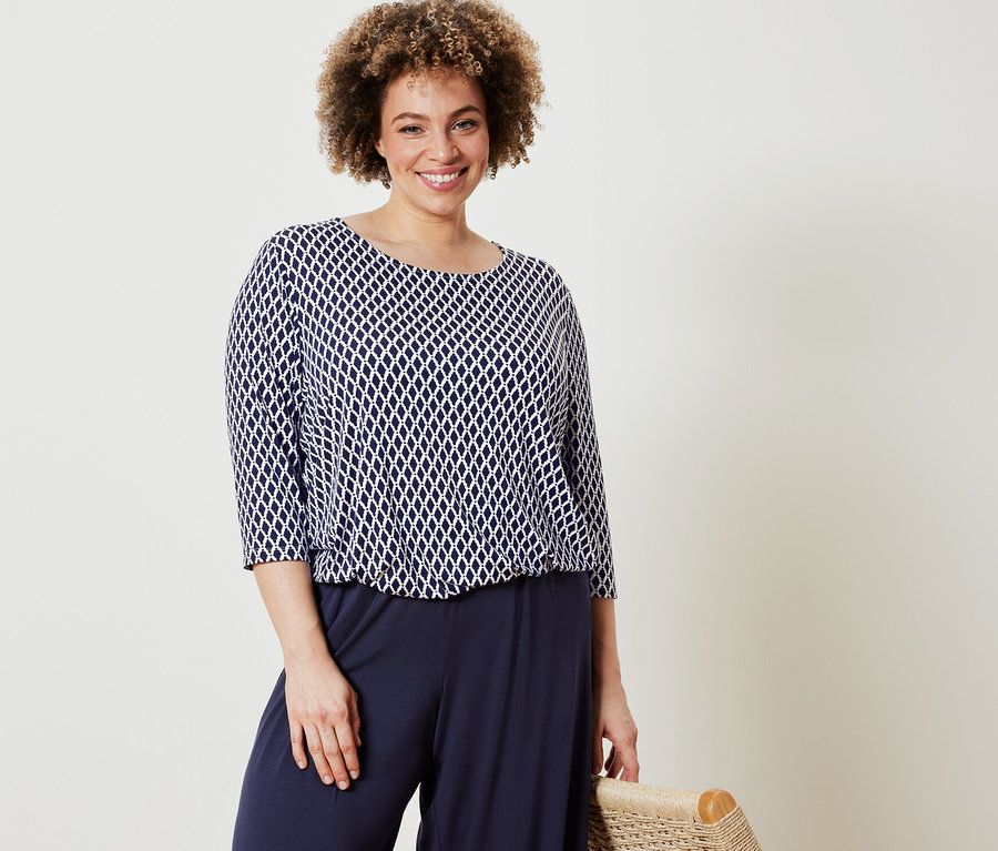 Kobieta pozuje w wzorzystej bluzce i granatowych spodniach palazzo.
