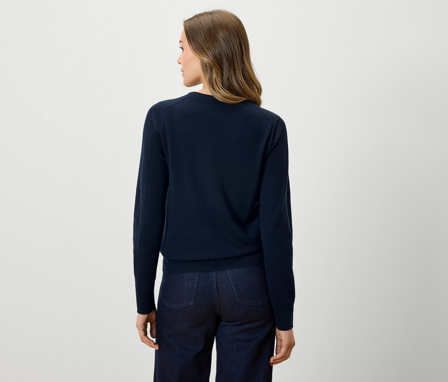 Widok z tyłu kobiety w granatowym swetrze i ciemnych dżinsach.