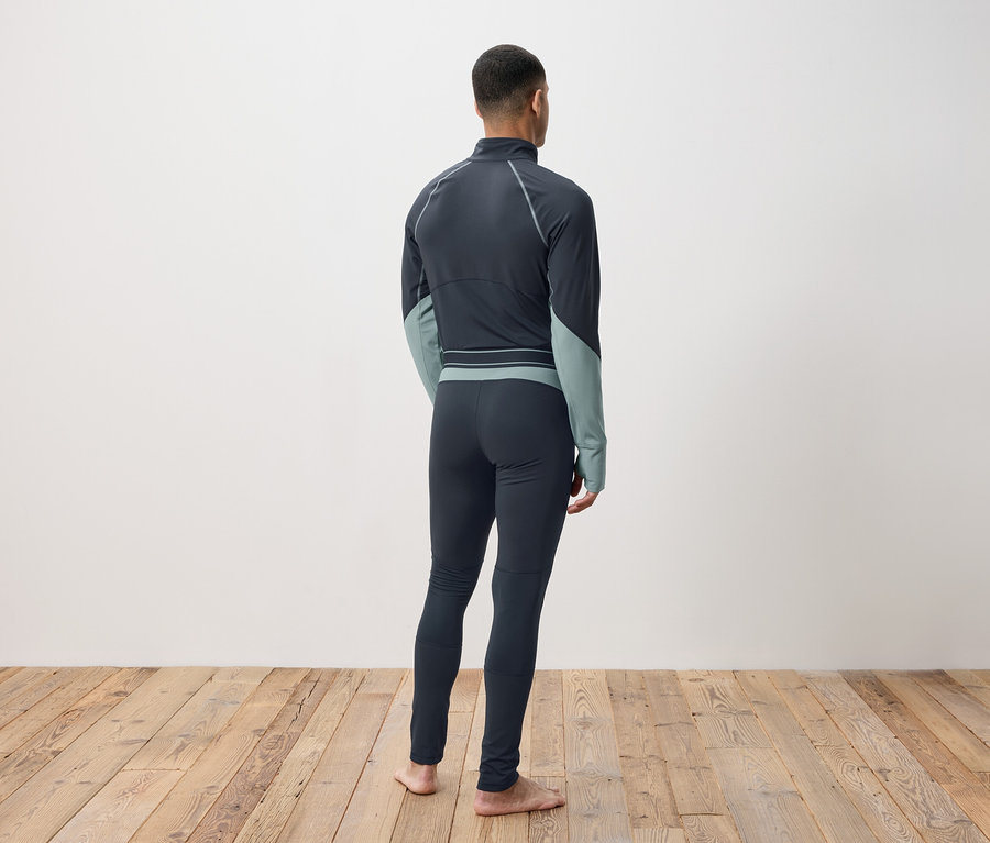 Mężczyzna tyłem do kamery w ciemnoszarej bieliźnie termoaktywnej stojący na drewnianej podłodze.