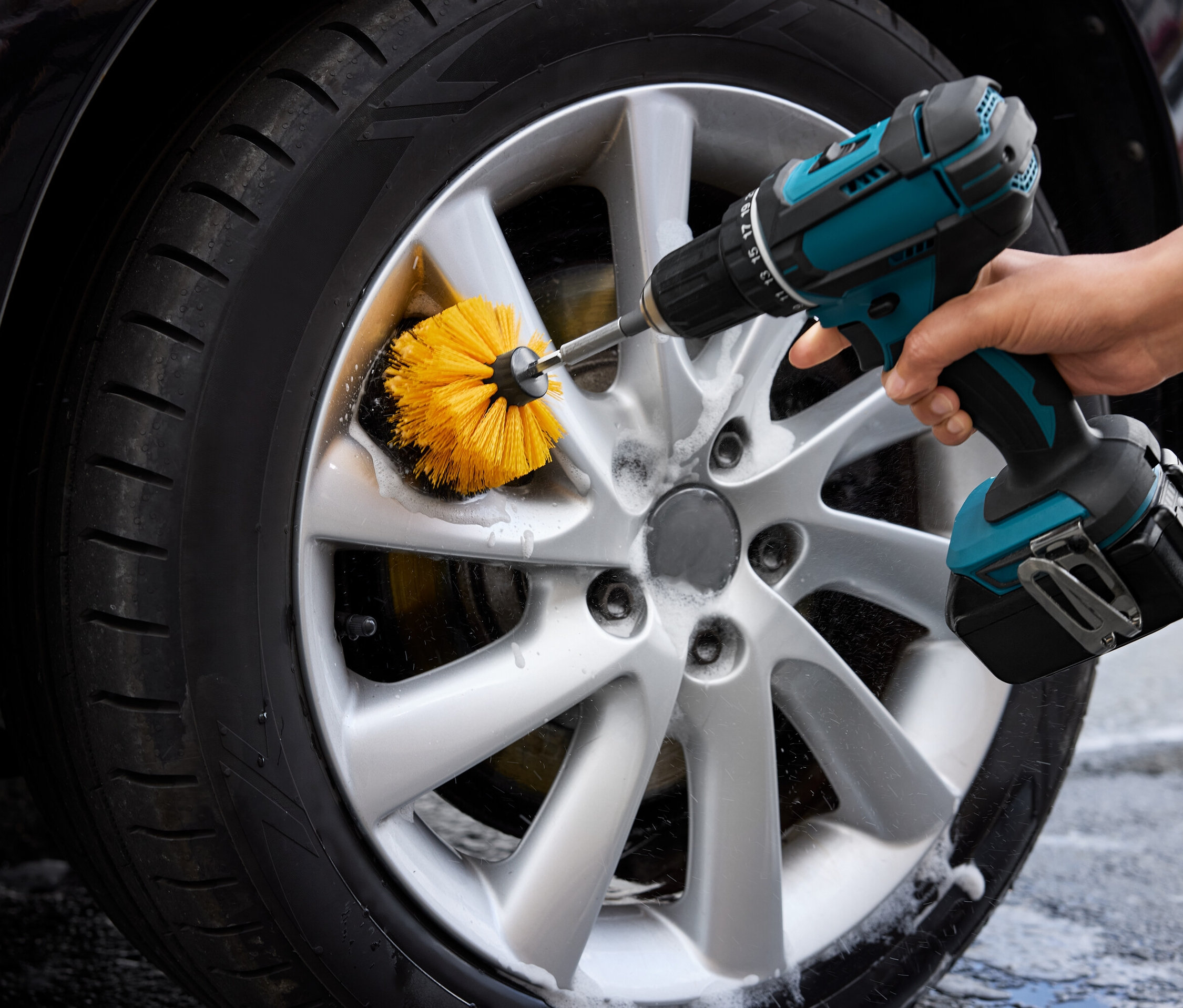 Mężczyzna czyści koło samochodu żółtą szczotką przymocowaną do wiertarki.