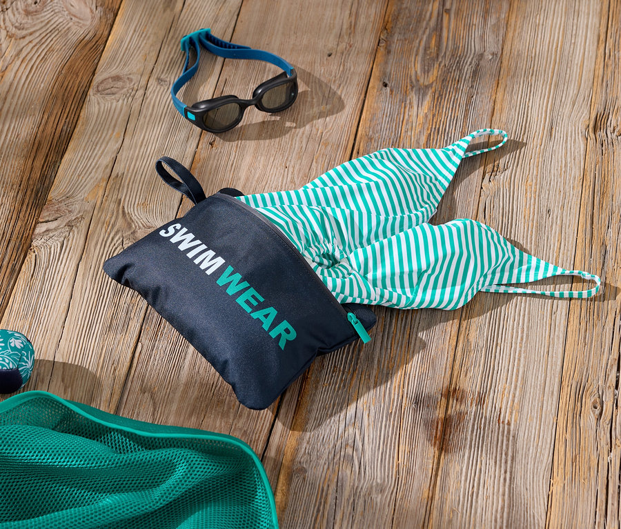 Zdjęcie akcesoriów pływackich na drewnianej powierzchni, w tym torby z napisem „Swimwear”, zielono-białego kostiumu kąpielowego w paski, okularów pływackich i zielonej siatki.