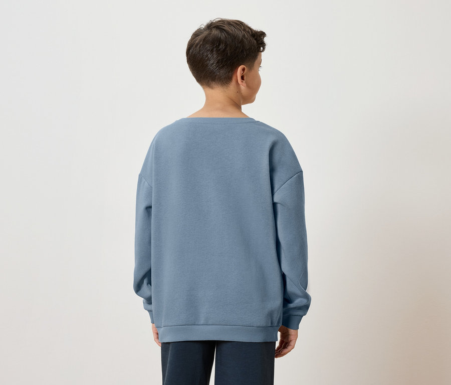 Tył chłopca z brązowymi włosami w niebieskiej bluzie i ciemnych spodniach na białym tle.