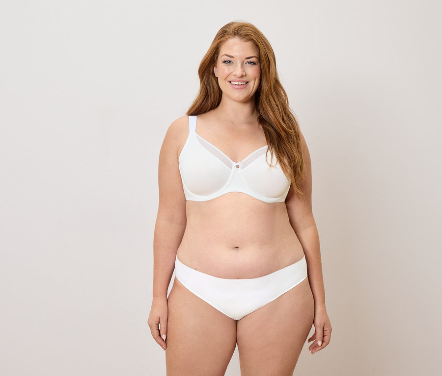 Uśmiechnięta kobieta z długimi rudymi włosami w białym biustonoszu i majtkach.