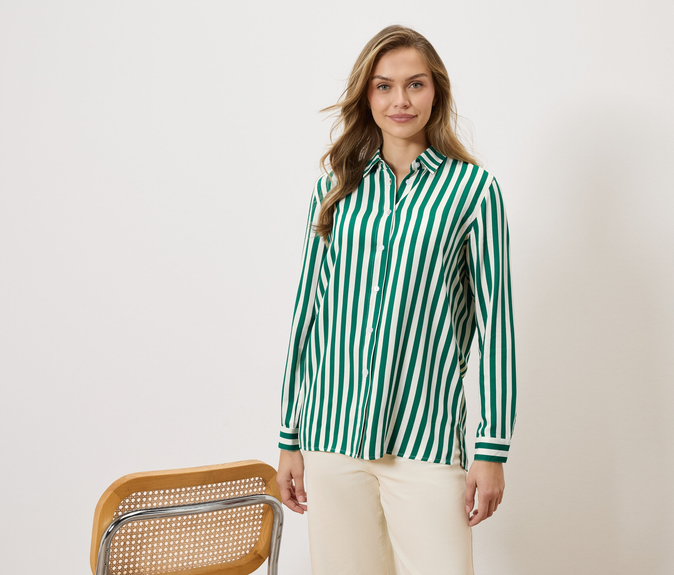 Kobieta nosi koszulę w zielono-białe paski i beżowe spodnie, obok krzesła.