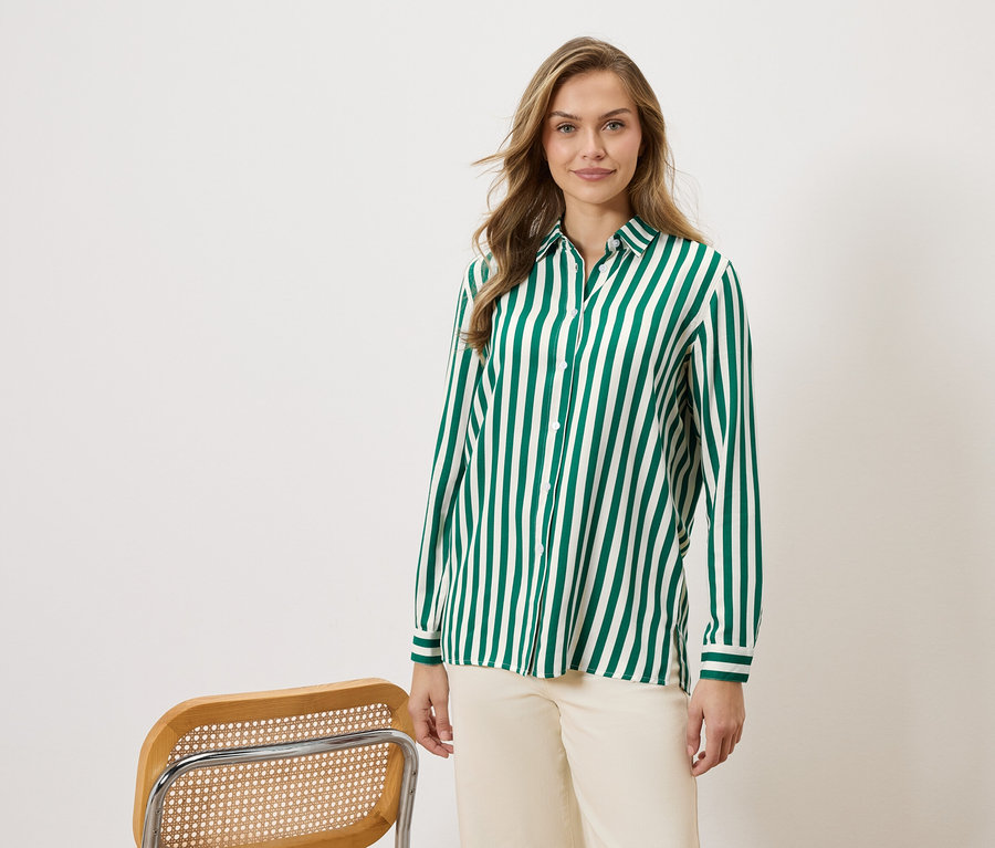 Kobieta nosi koszulę w zielono-białe paski i beżowe spodnie, obok krzesła.