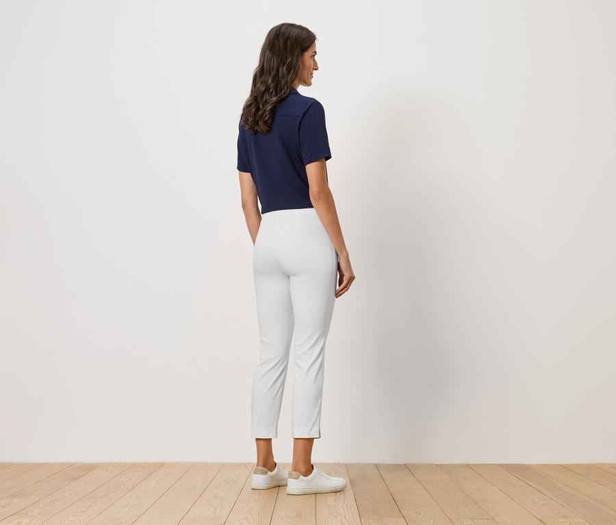 Kobieta stoi tyłem do kamery, ubrana w granatową koszulkę polo, białe spodnie i białe buty.