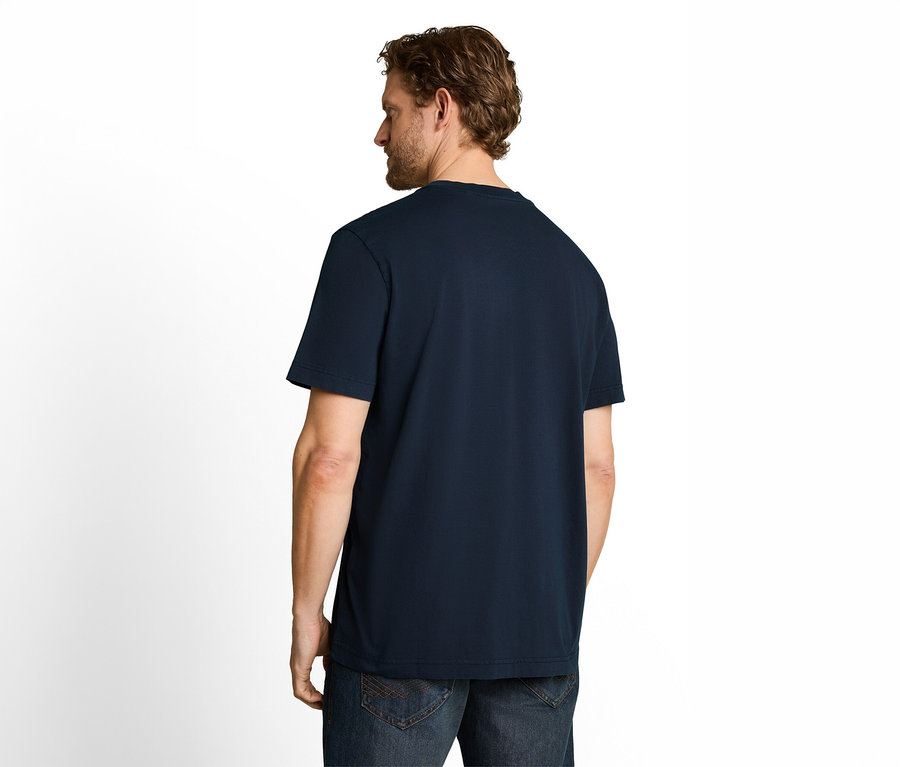 Mężczyzna widziany od tyłu, ubrany w granatowy T-shirt i jeansy, patrzący w lewo. Ma krótkie brązowe włosy i brodę.