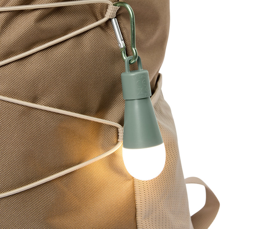 Zbliżenie oliwkowozielonej lampki LED przymocowanej karabińczykiem do beżowego plecaka.