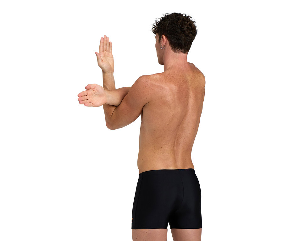 Mężczyzna rozciąga ramiona, ma na sobie czarne kąpielówki.