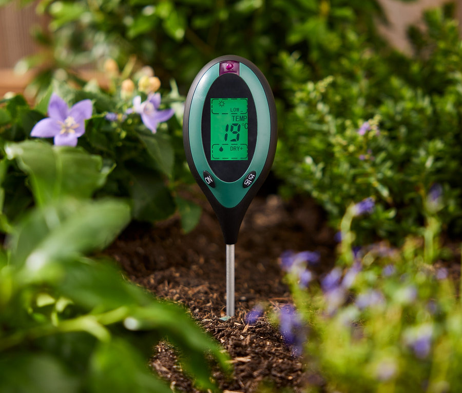 Zielony miernik gleby wbity w ziemię między roślinami.