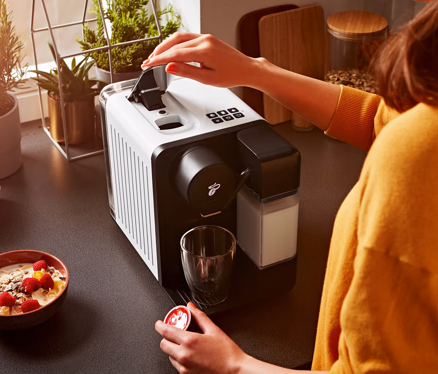 Kobieta otwiera biały ekspres do kawy Cafissimo milk i trzyma kapsułkę.