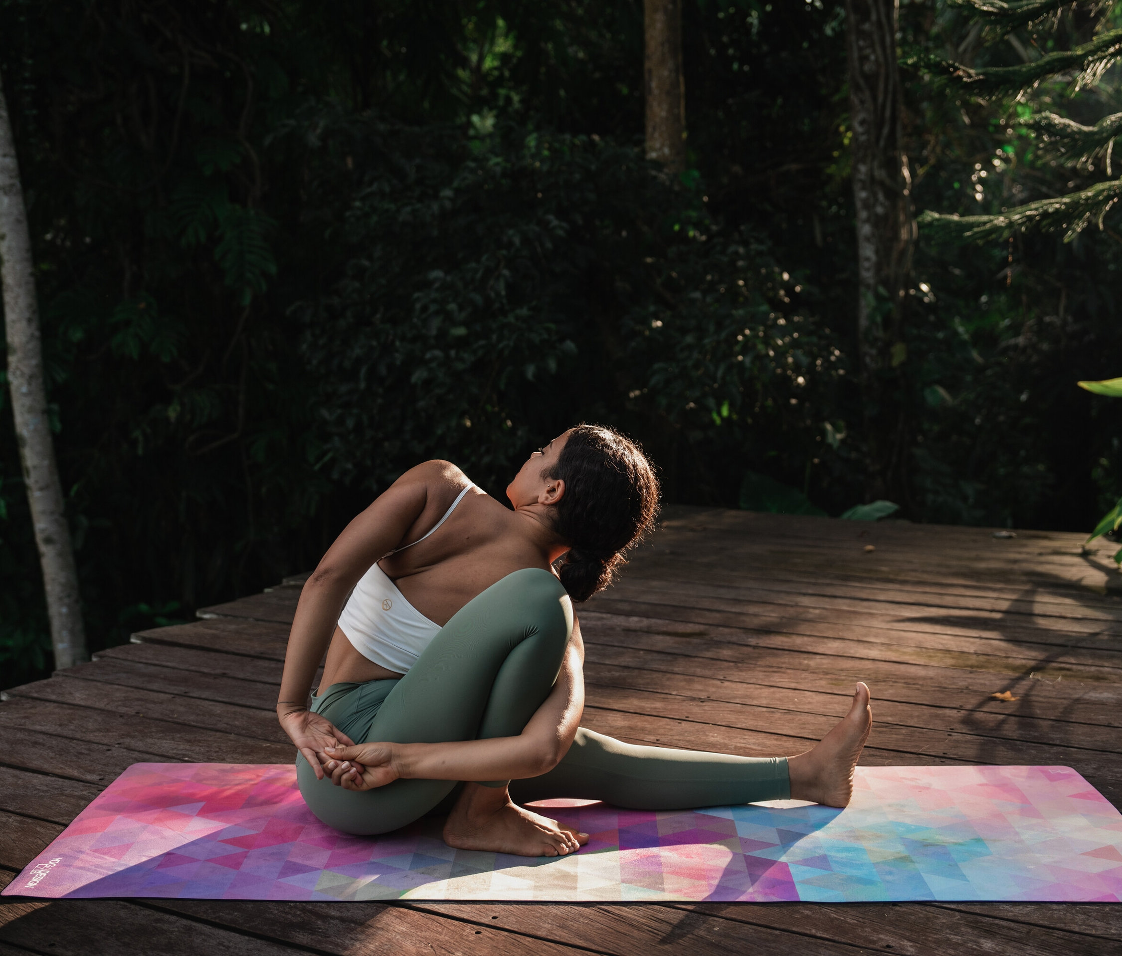 Kobieta ćwiczy jogę na kolorowej macie na drewnianej podłodze.